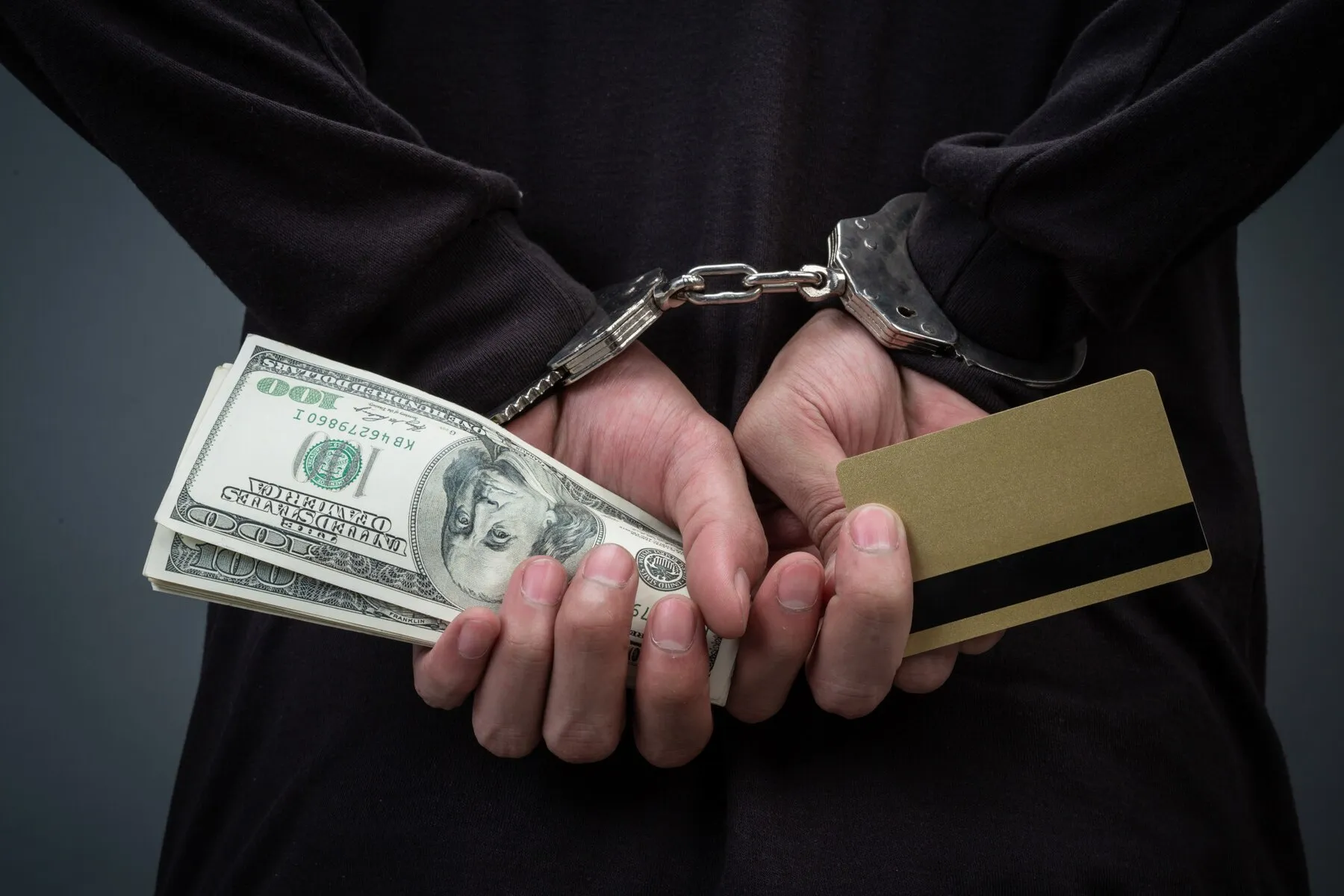 Individual handcuffed showing money and credit card behind his back.