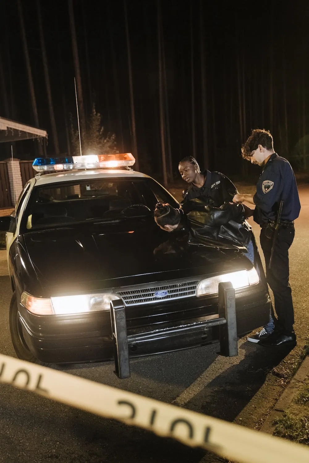 Two police officers arresting an individual and place him face down on a cop car.
